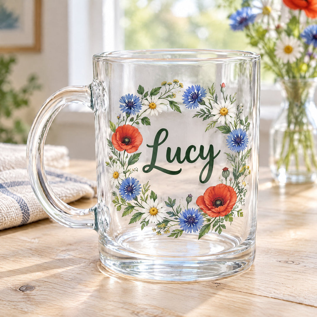 11oz glass sublimation mug printed with a poppy and cornflower wreath around the name Lucy, on a wooden table by wildflowers