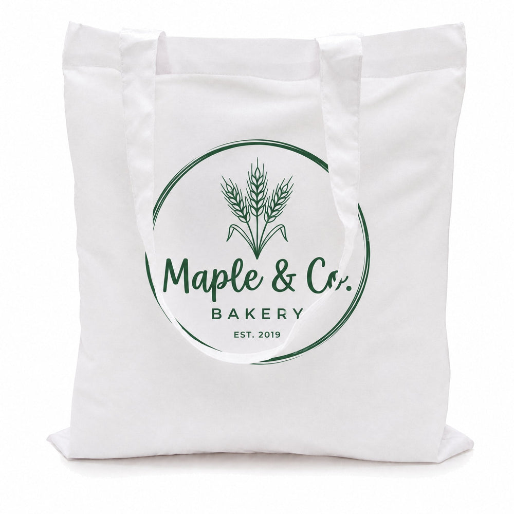 White cotton tote bags printed with a green wheat-sheaf logo reading 'Maple & Co. Bakery, Est. 2019'